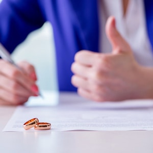 A woman signing a prenup with wedding rings on it