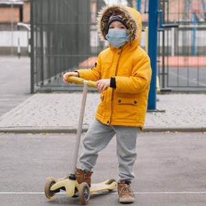 A child wearing a mask playing on a scooter signifying negotiating child custody during COVID-19