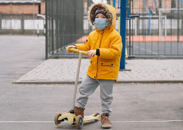 A child wearing a mask playing on a scooter signifying negotiating child custody during COVID-19