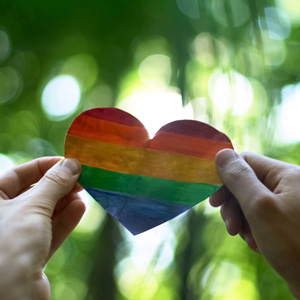 2 hands holding up a rainbow colored heart