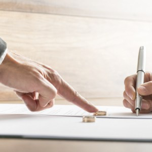 Hands and marriage rings on divorce papers where a woman is signing them