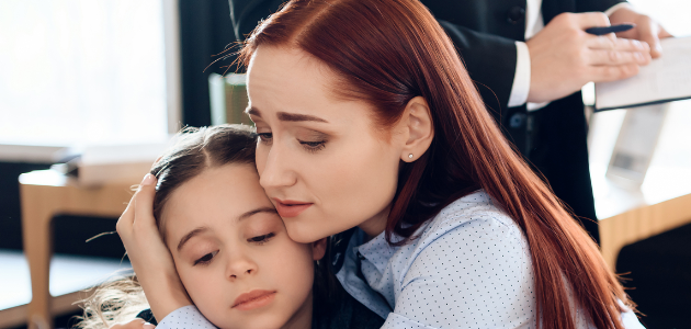 Red haired woman hugs upset girl sitting in lawyer's office.