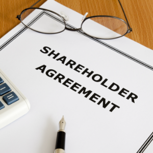 Shareholder agreement reviewed in a business owner divorce involving company ownership and asset division with glasses, a pen and a calculator